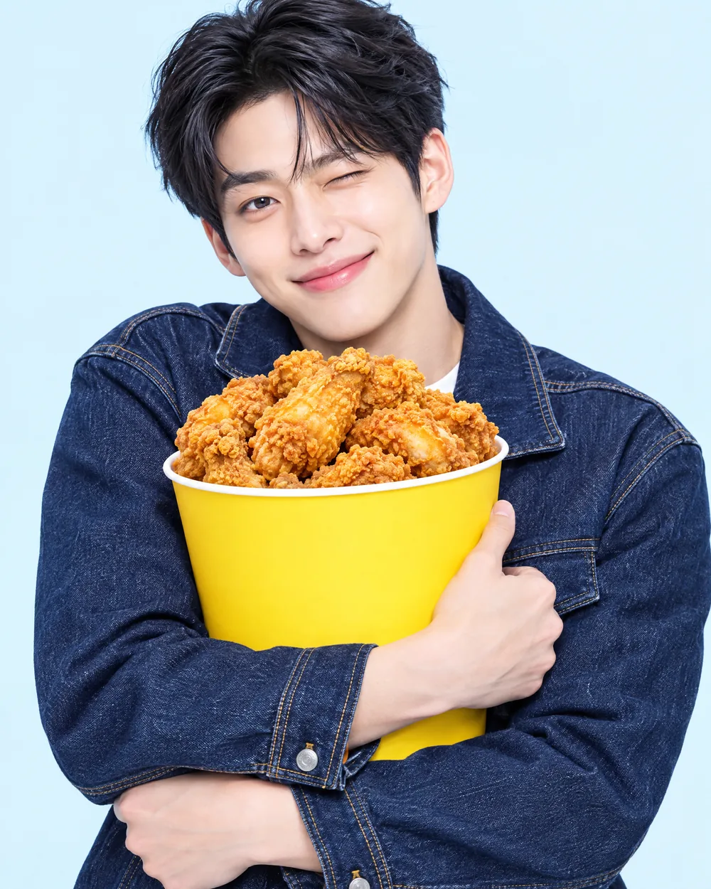인디고 데님 차림의 남성이 노란 치킨 버킷을 안고 윙크하는 모습